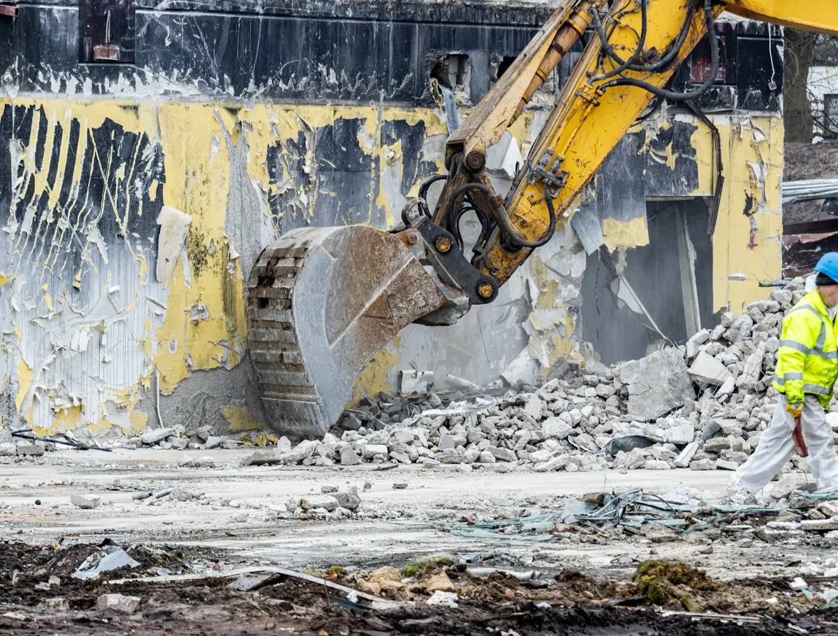 Arbeiter mit Warnweste auf einer Rückbau-Baustelle neben einem Bagger